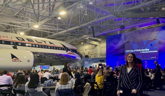 Packed air hangar with a delta plane and a screen setup that reads "2020 Day of Understanding." 