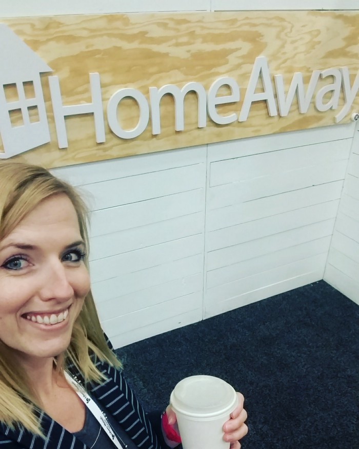 Blonde woman holding a coffee and smiling at camera posing with HomeAway sign