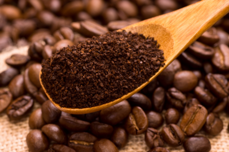 scoop of ground coffee above coffee beans