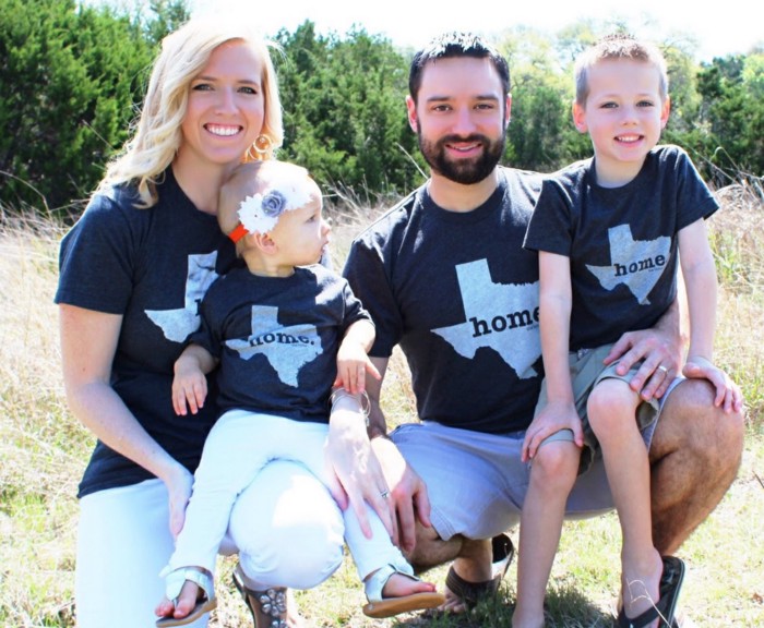 Family of four smiling at camera wearing dark blue shirts that say home in the Texas shape