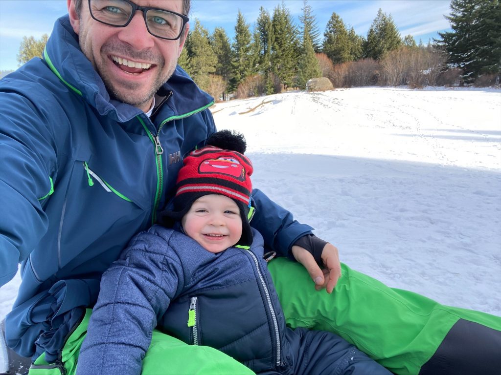Man smiling with glasses with a small child in his lap on the snow