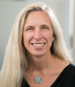 Woman with long blonde hair smiling and wearing a teal pendant necklace